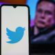 Twitter logo on smartphone and Elon Musk in the background | Elon Musk Declines Chance to Join Twitter Board