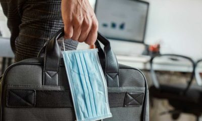 closeup of a young man in an office holding a briefcase and a surgical mask in his hand | Go Back to the Office Or Quit? 64% Of Workers Say They’ll Quit | featured