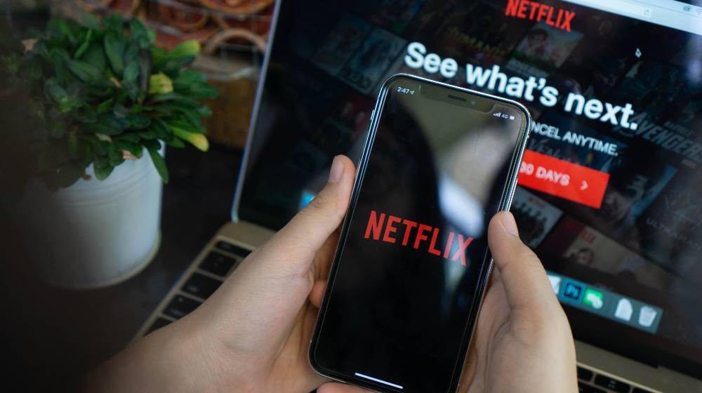 man using IPhone X with Netflix application set on screen | Netflix Lost 200,000 Subscribers, Blames Password Sharing | featured
