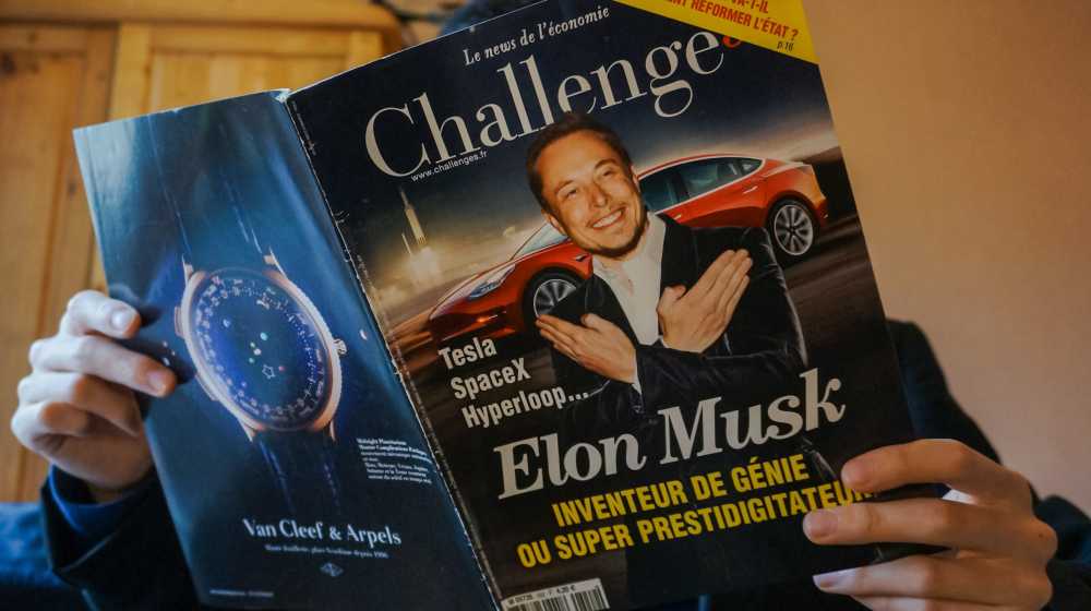A man reads an issue of the French economic newspaper Challenges showing the businessman Elon Musk in front of a Tesla | Biden’s Tweet About US Auto Manufacturing Ignores Tesla, Elon Musk | featured