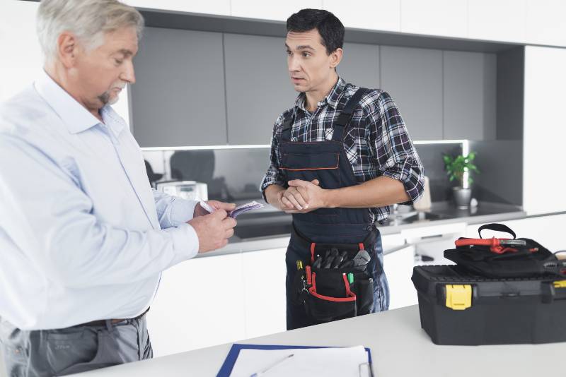 A plumber man communicates with a client who pays for the work done | Home Repairs