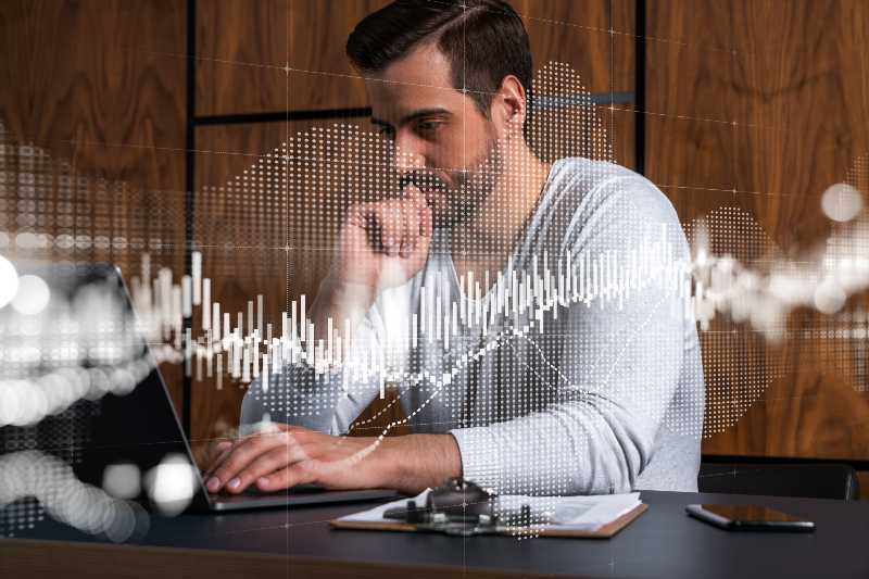 A serious caucasian analyst in casual wears, using laptop to proceed the forecast of stock market behavior | Understanding Your Investing Behavior, with Tom Gardner and Morgan Housel