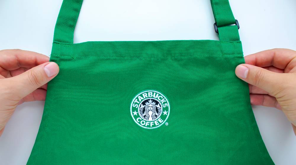 An Starbucks employee holding a store branded apron | Buffalo, NY Starbucks Workers Vote To Form 1st Union | featured
