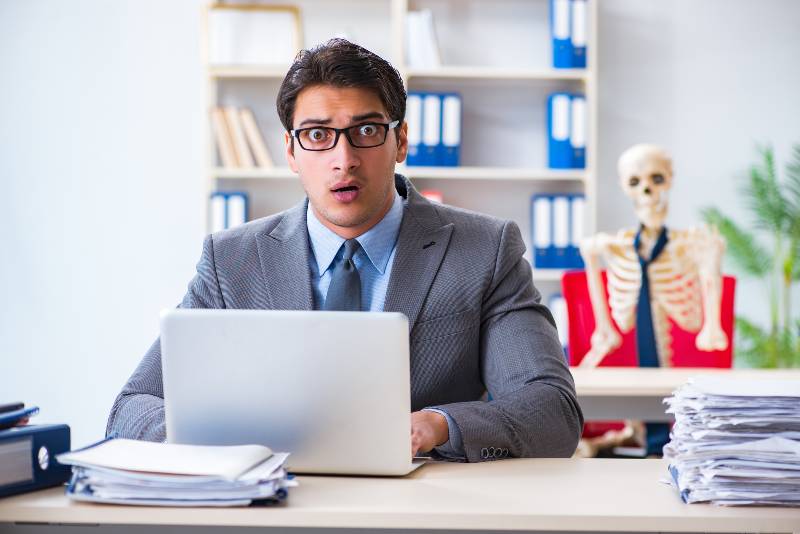 Businessman working with skeleton in office-Halloween Stocks