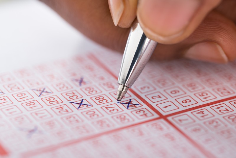 Close-up Of Person's Hand Marking Number On Lottery Ticket With Pen | Lottery Alternatives