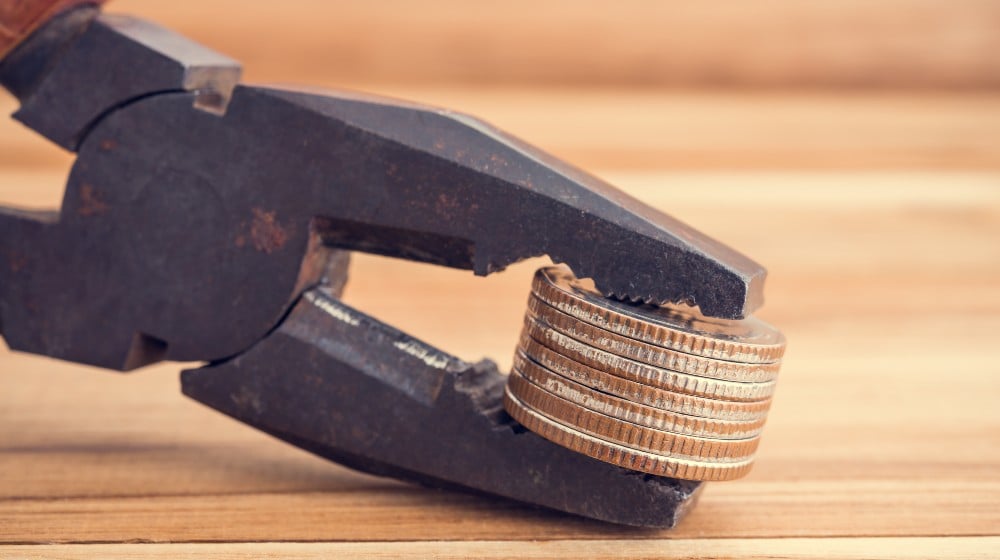 Coins tightened up in plier clamp. Inflation, economy or financial crisis, trade war concept | Rise in Wages Seen To Increase Inflation Concerns | featured