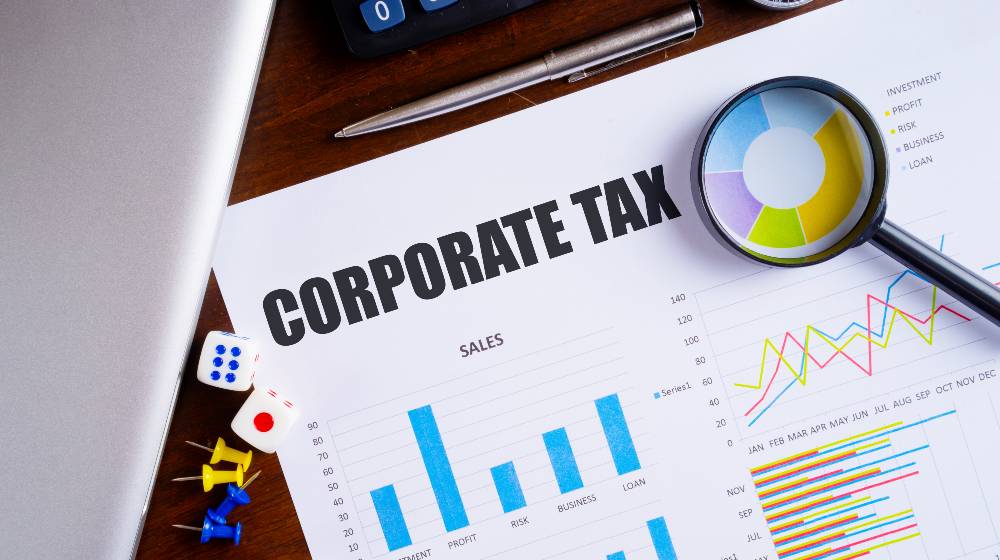 Corporate Tax text on paper sheet with magnifying glass on chart | Democrats Want The Corporate Tax Rate Up From 21% To 26.5% | featured