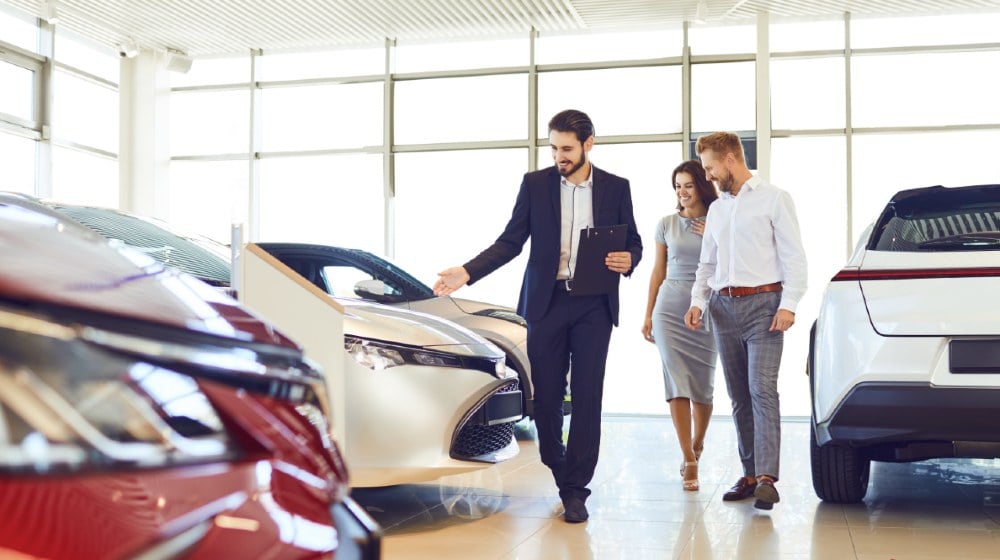 Couple and the dealer selling cars look the car in the showroom-US Auto Sales-ss-featured