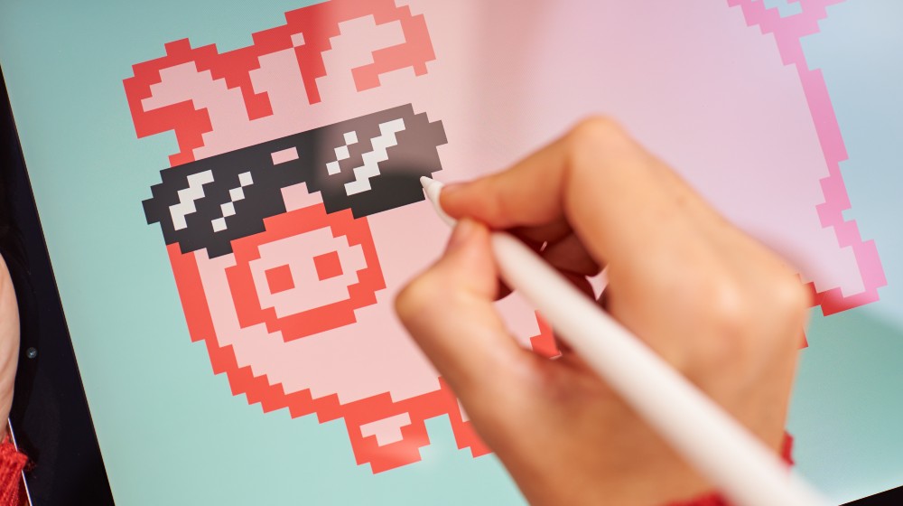 Female artist painting digitally on a tablet creating NFT | Can I Create My Own Cryptocurrency? | featured