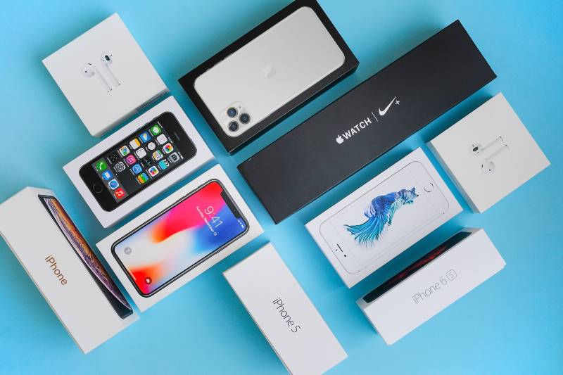 Flat lay of different generation of iPhone smartphone boxes iPhones, headphones, watches are on a blue background | Apple Products Are Not Available In Russia