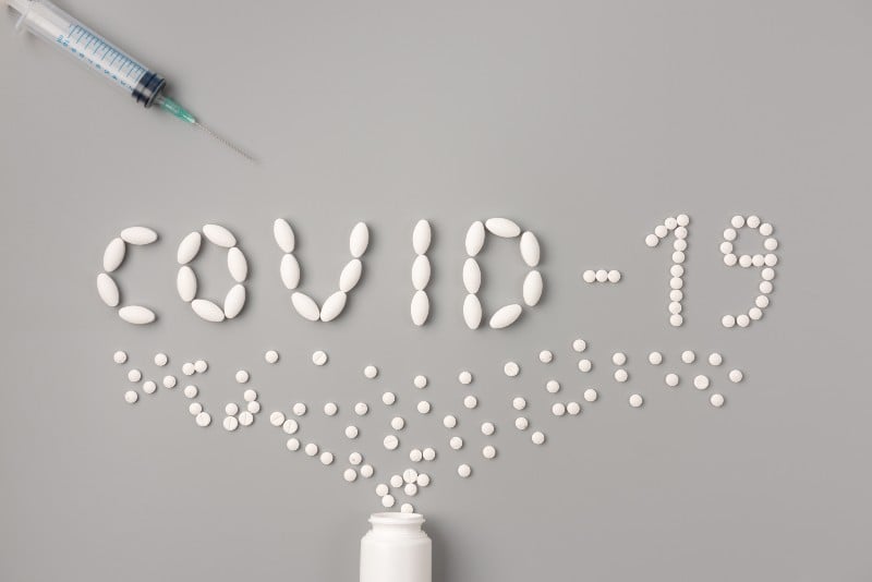 Flat lay of medicine pills shape as word covid 19 with syringe and pills | COVID Pill