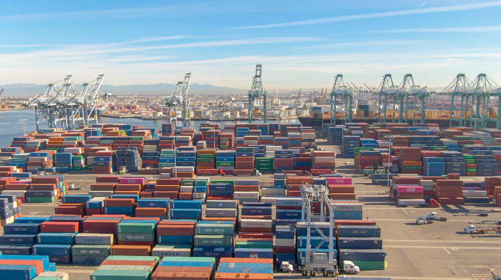 Flying over the massive freight dockyard in Los Angeles on a sunny day | Cargo Delays Pile Up As California Ports Stay Clogged | featured