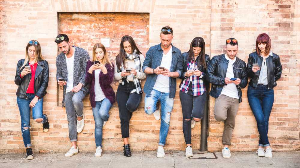 Friends group using smartphone against wall at university college backyard break | Tech firms in new battle for millennials | featured