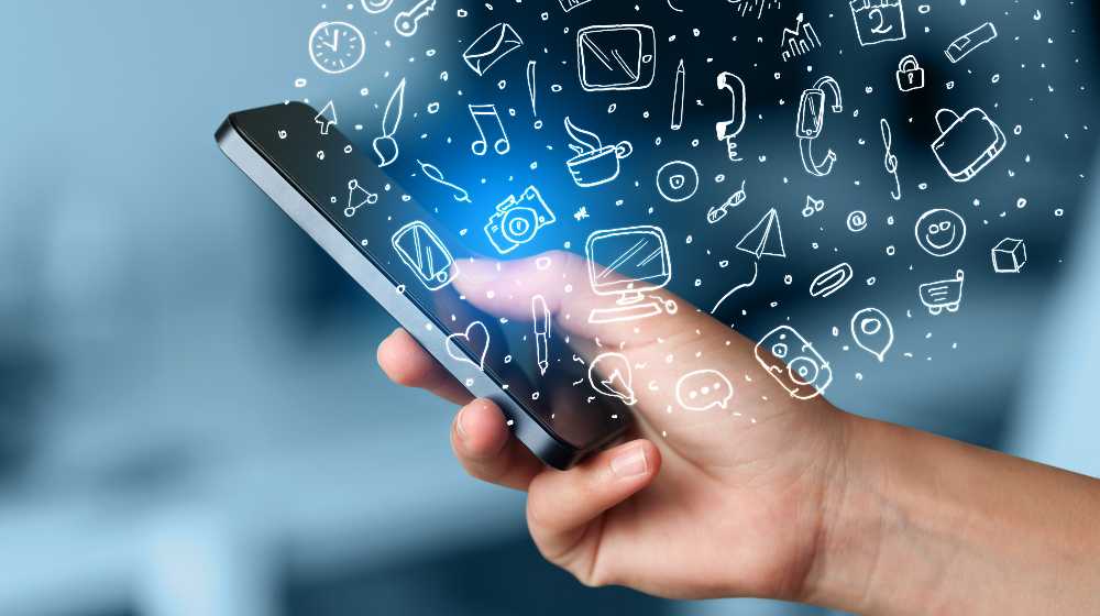 Hand holding smartphone with hand drawn media icons and symbols concept | Things to Consider While Choosing A Mobile App Development Company | featured