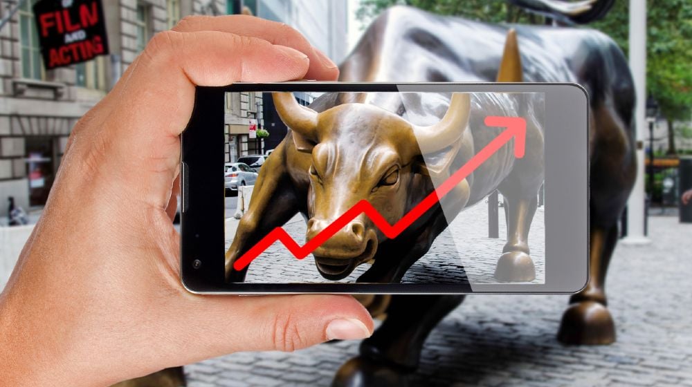 Hand pointing smartphone screen at bull of wall street in New York showing growing stock chart-Wall Street Record Highs-ss-featured