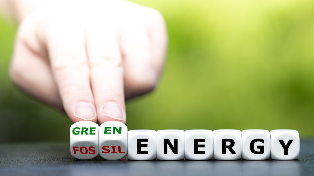 Hand turns dice and changes the expression fossil energy to green energy | Green Energy Stocks Dip due to high interest rates