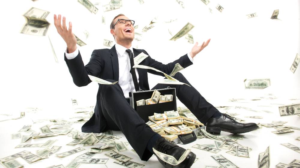 I am rich! Happy young businessman in formalwear throwing money up while sitting | World’s 10 Richest Men Doubled Their Wealth During The Pandemic | featured