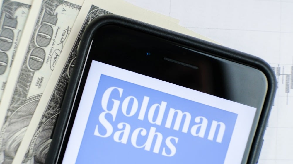 Logo of the Goldman Sachs Group in the smartphone lying on paper with charts and one hundred dollar bills-Goldman Sachs Advice-ss-featured