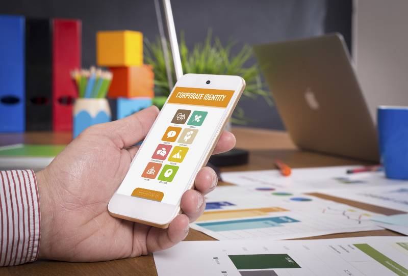 Man showing smartphone Corporate Identity on screen | Things to Consider While Choosing A Mobile App Development Company