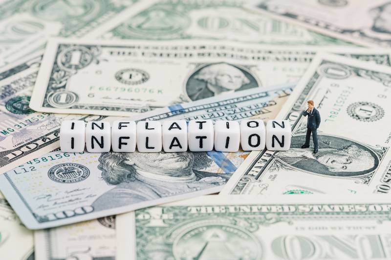 Miniature people businessman standing and wise thinking with cube block combine word Inflation on US dollar money banknote | How to Stretch Your Budget When Inflation Hits