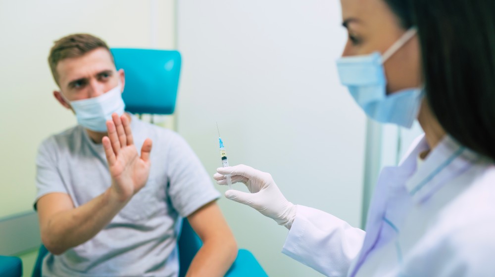 No Vaccination. Scared Man Gesturing Stop To Hand Offering Syringe With Vaccine Refusing To Be Vaccinated
