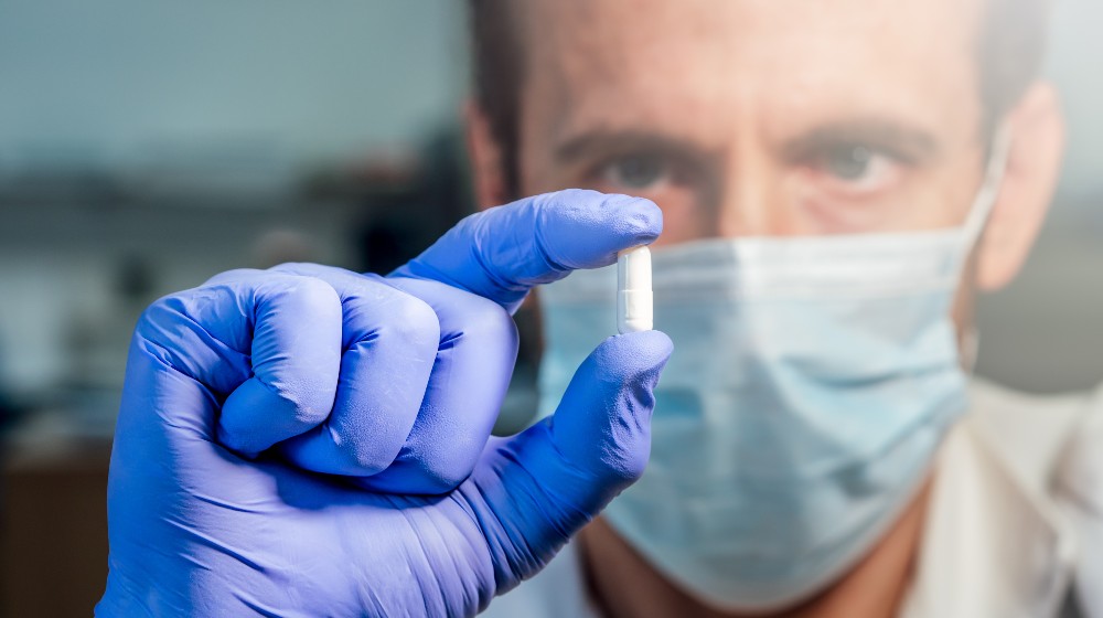 Scientist with medical mask showing white pill | Pfizer Files for FDA Approval for Its COVID Pill | featured