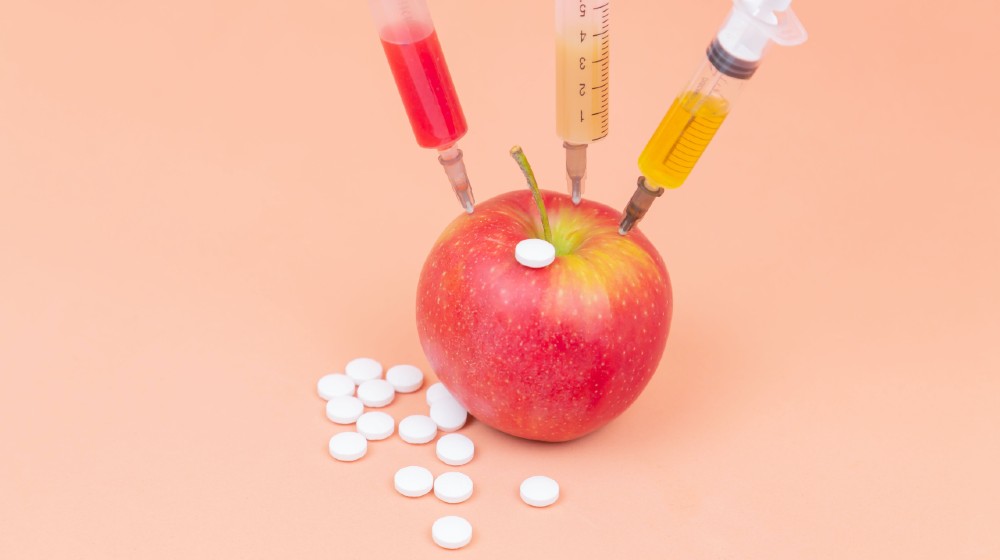Syringes with different chemicals injections and tablets in a red apple on an orange background | How COVID-19 Impacting AI for Drug Discovery Market | Featured