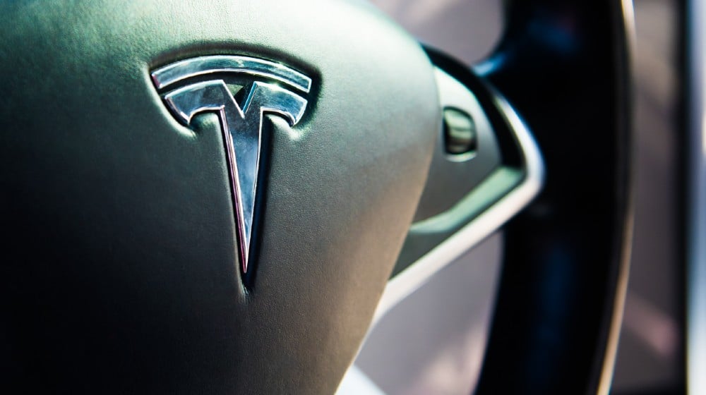 Tesla logo on black leather luxury electro mobile car steering wheel | Tesla Recalls Vehicles Over Seat Belt Safety Issues | featured