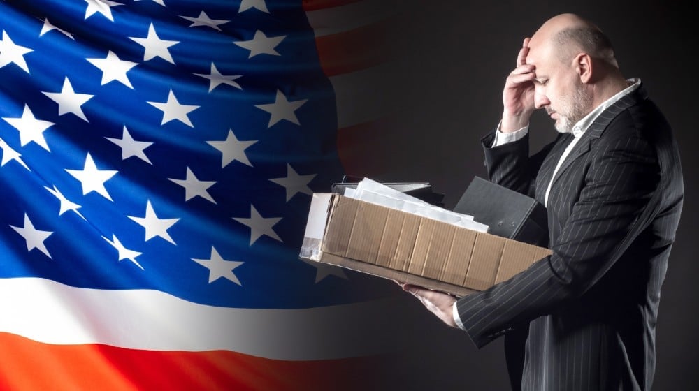 The dismissed employee clutched his head against the background of the US flag-Weekly Jobless Claims-ss-featured
