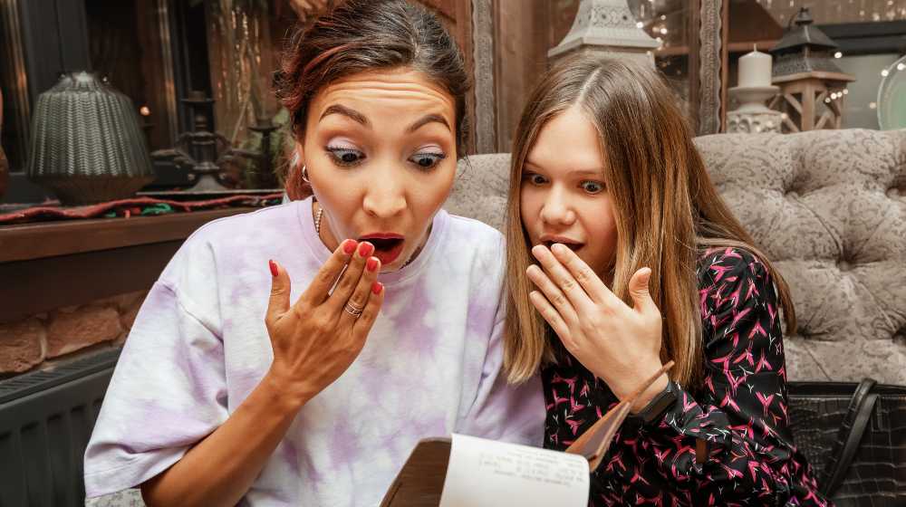 Two girls are surprised and shocked by the final bill for dinner at the restaurant. The concept of price increases and currency inflation | Are Corporations Using Inflation To Raise Prices Excessively? | featured