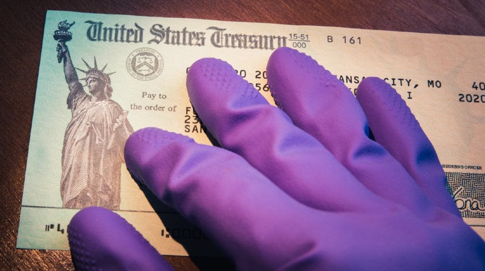United States Treasury check being held by rubber glove illustrates US Government coronavirus economic impact payment sent-Second Stimulus Check-ss-Featured
