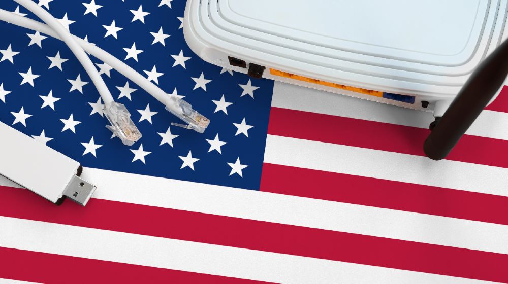 United States of America flag depicted on table with internet rj45 cable, wireless usb wifi adapter and router | Big Tech Wary Of Biden’s $100B ‘Broadband for All’ Plan | Featured