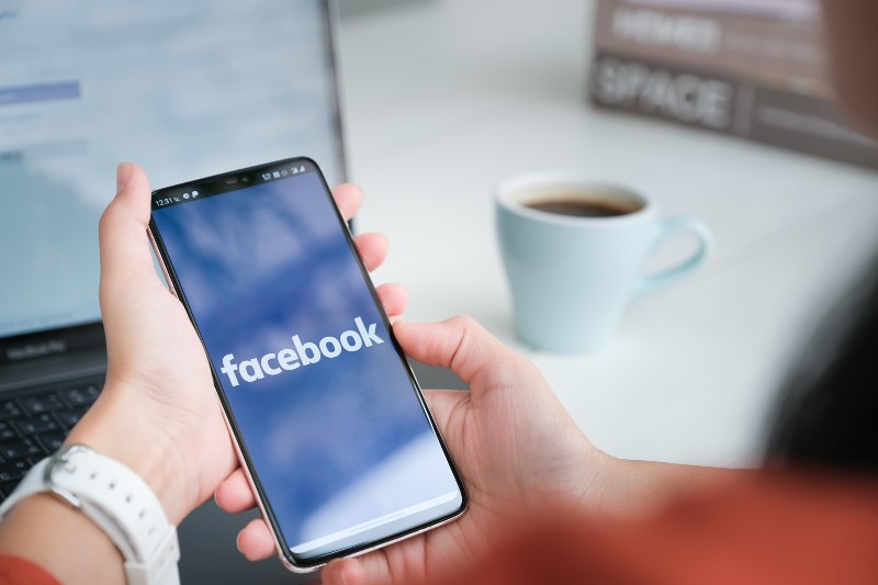 Woman holds smart phone with facebook application on the screen-Facebook Rebrand