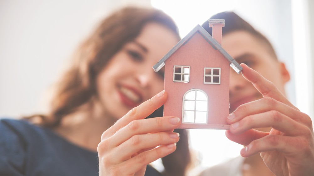 Young loving couple with small wooden house new home concept | Lessons Learned From Home Ownership | featured