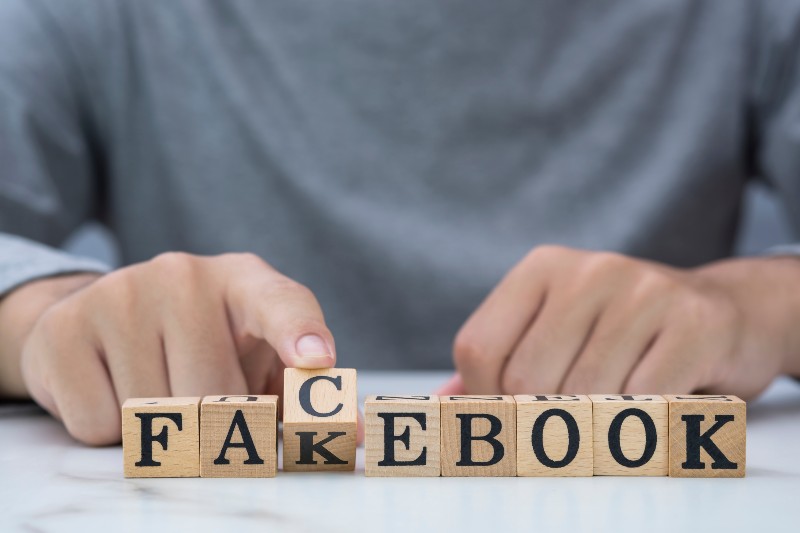 Young man's hand flipping wooden cubical blocks for change fakebook to facebook wording-facebook