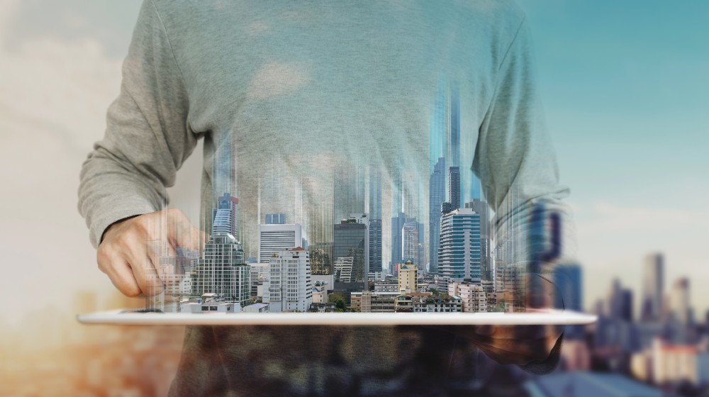a man using digital tablet, and modern buildings hologram | Two Reasons Why Property Technology Is Suddenly Super Hot | featured