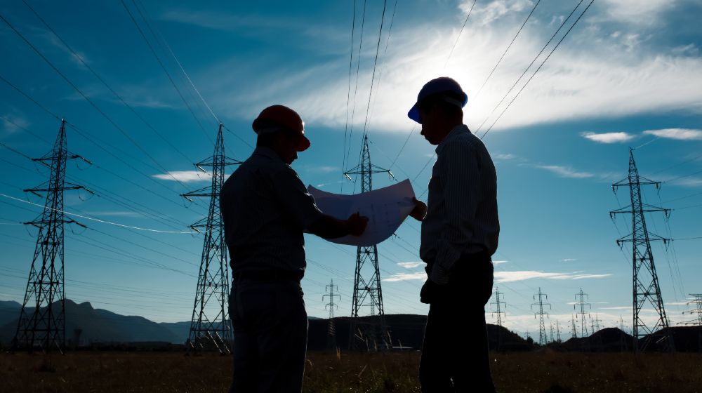 silhouette of two engineers standing at electricity station | Biden, Senators Agree To $1T Bipartisan Infrastructure Deal | featured